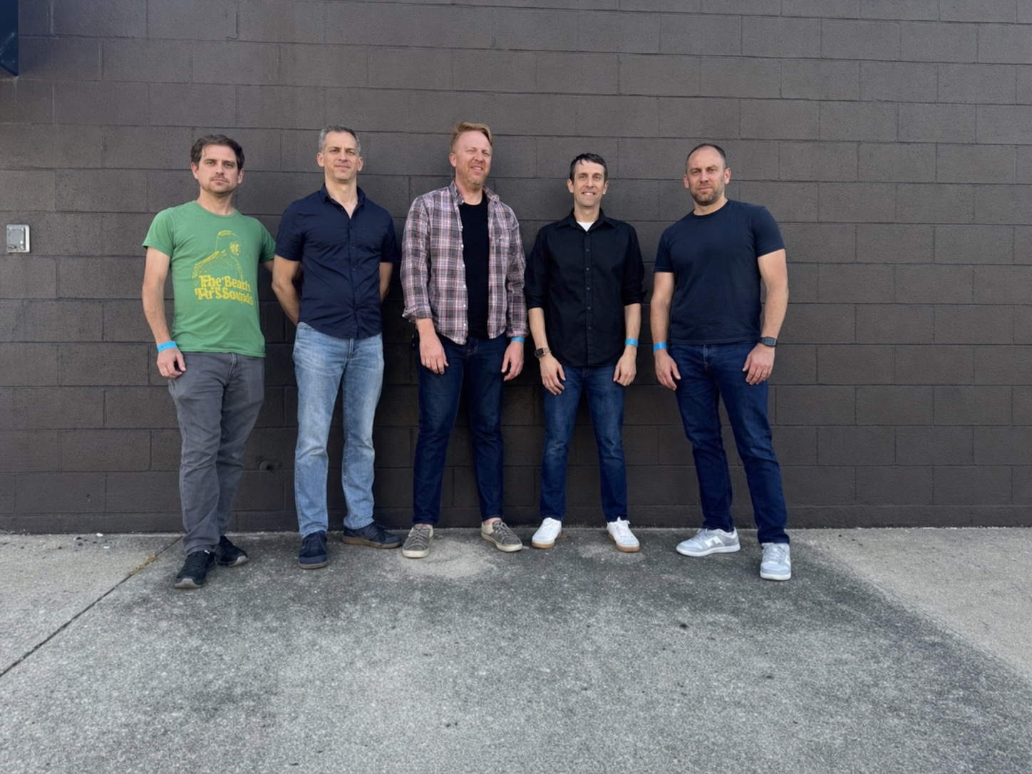 The five members of The Whiles together in front of a dark brick wall